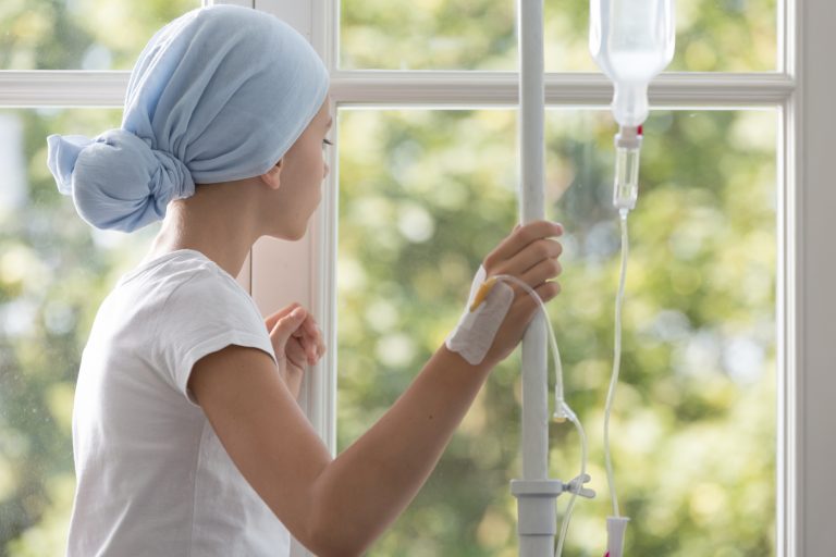 Mulher com câncer usa lenço na cabeça e toma medicação na veia enquanto olha pela janela